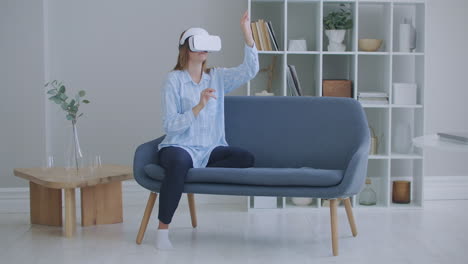 Porträt-Einer-Jungen-Frau-Mit-Virtual-Reality-Brille,-Die-Zu-Hause-Auf-Dem-Sofa-Sitzt.-Junges-Mädchen-Im-Virtual-Reality-Headset-Scrollt-In-Der-Luft-Zu-Hause,-Technologiekonzept.